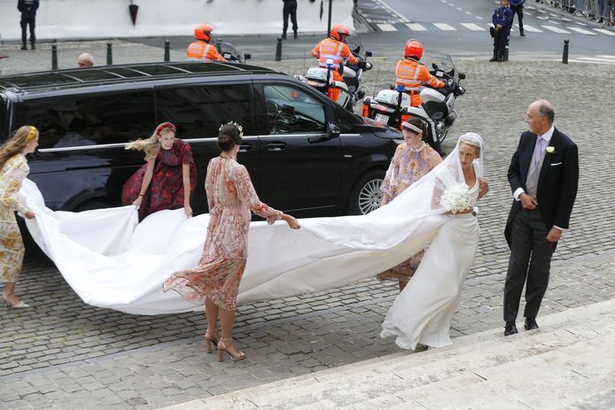 The bride gets out of the car. She wears a diamond tiara and a four-meter train.